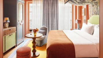 A hotel room with a large bed, a round table, a chair, a wardrobe, and a decorative ceiling light.