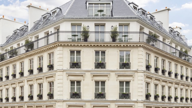 A multi-story hotel with a classic European architectural style, featuring balconies with potted plants, a ground-level café with outdoor seating, and a prominent awning. - Hotel Le Grand Mazarin (Paris)