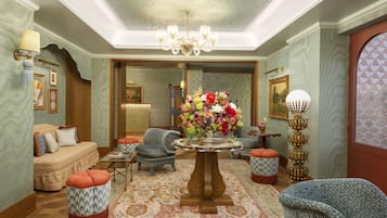 A spacious living room with a central round table, comfortable seating, and a large mirror reflecting the room.