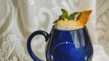 A blue mug with a decorative design, filled with a beverage and garnished with a mint leaf and a piece of bread.