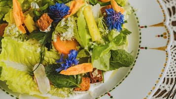 Un piatto di insalata con diverse verdure e fiori su un piatto bianco con bordo decorativo.