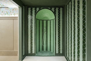 A bathroom with a green-tiled shower area, a tiled floor, and a decorative ceiling.