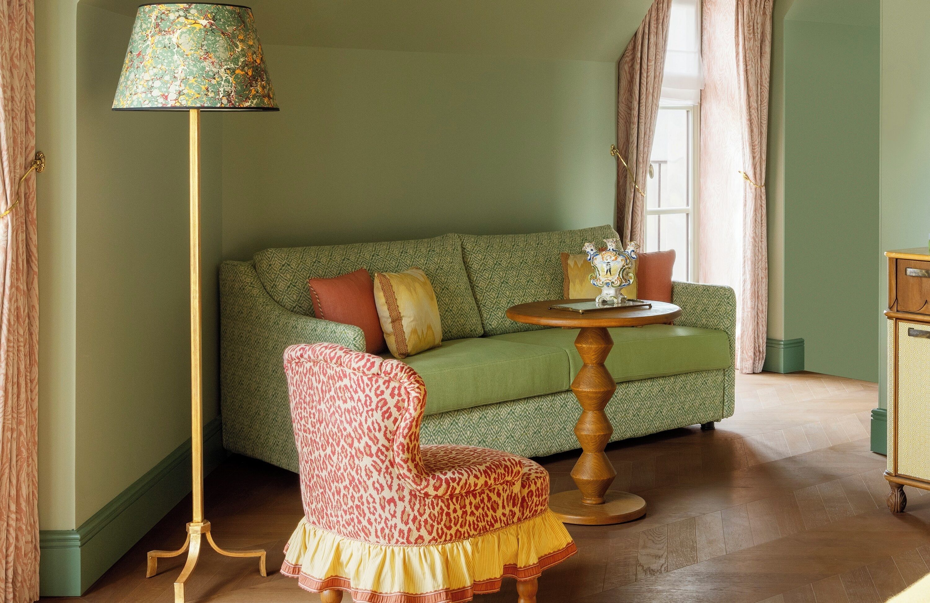 A room with a green sofa, a leopard print chair, a wooden table, and a floor lamp.