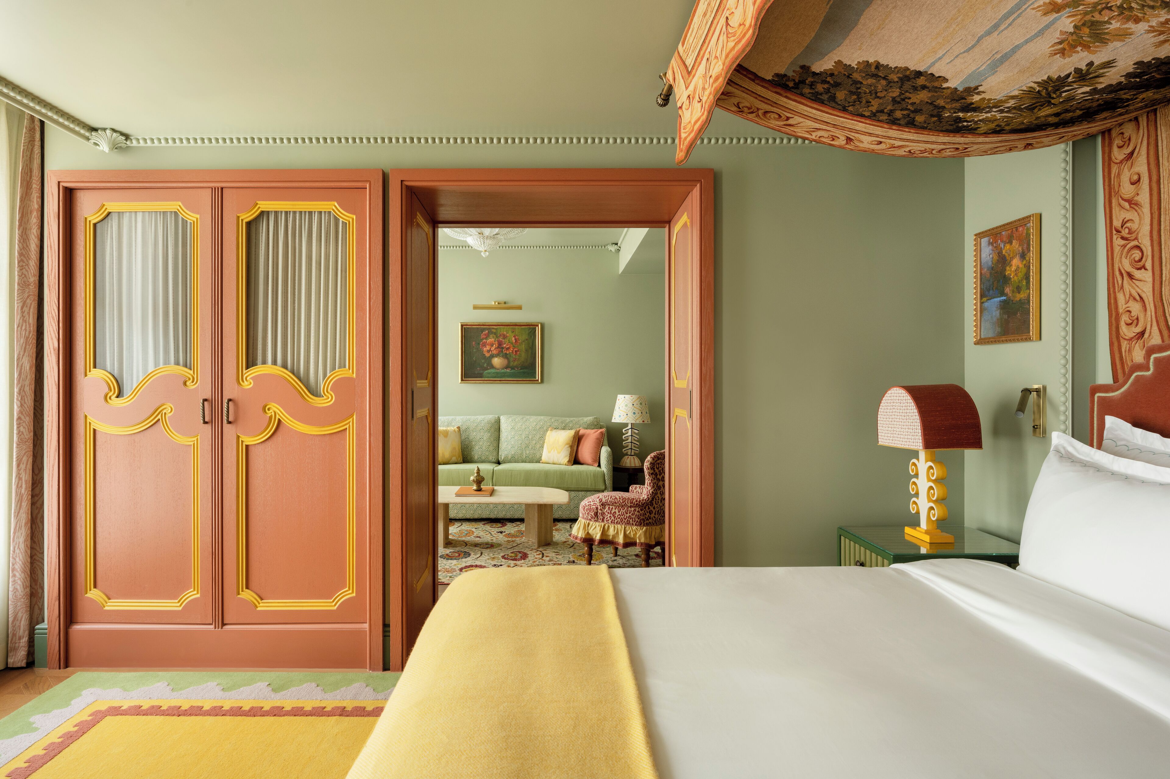 A hotel room with a bed, a green sofa, a chair, a lamp, and a door with decorative panels.