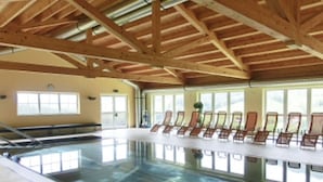 An indoor swimming pool with wooden beams, sunlit windows, and lounge chairs along the poolside. - "Almhaus Kleeblatt" cozy vacation home - dreamlike in the ski and hiking area (Annaberg)