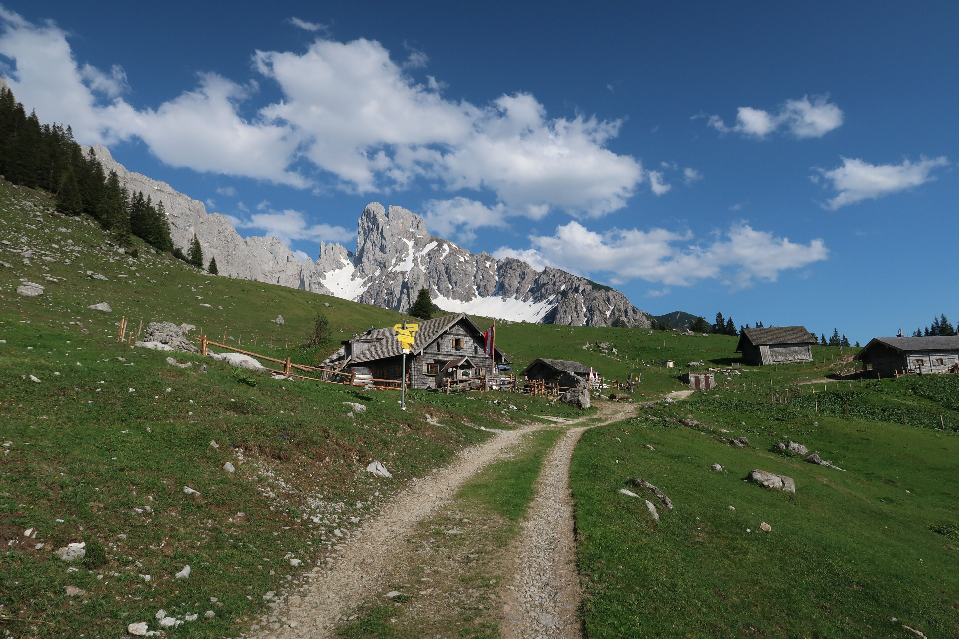 A rural mountain road leading to traditional wooden houses with a clear view of a rocky mountain range.