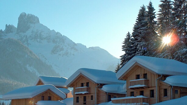A row of wooden cabins with snow-covered roofs and balconies, surrounded by snow-covered mountains and trees. - "Almhaus Kleeblatt" cozy vacation home - dreamlike in the ski and hiking area (Annaberg)