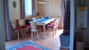 A wooden cabin with a dining area featuring a table and chairs, a window with curtains, and a ceiling light fixture. - "Almhaus Kleeblatt" cozy vacation home - dreamlike in the ski and hiking area (Annaberg)