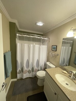 A bathroom with a shower curtain, toilet, sink, and a mirror.