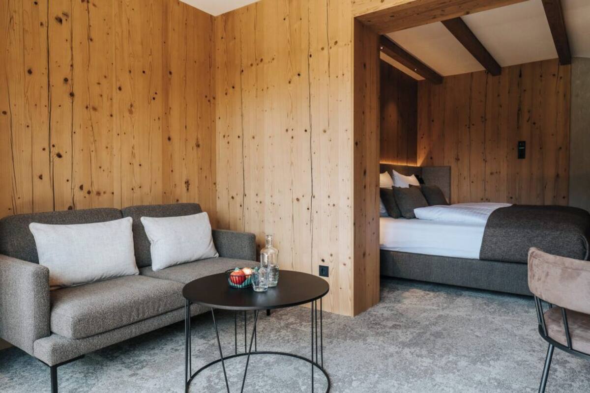 A cozy room with a grey sofa, a small round table, and a bed with grey bedding.