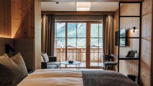 A hotel room with a large bed, a small table with chairs, a TV mounted on the wall, and a view of mountains through the window. - NOVA Moments Boutique-Hotel (Eben am Achensee)