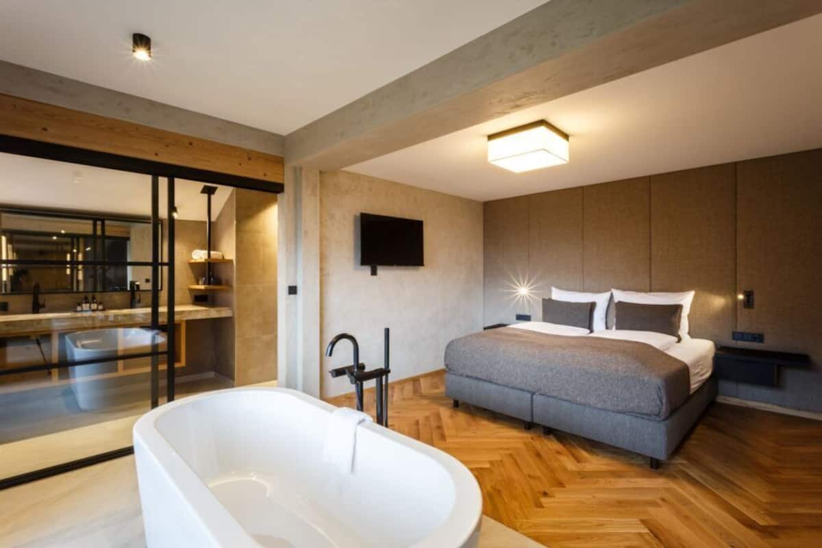 A modern bedroom with a large bed, a bathtub, and a television on the wall.