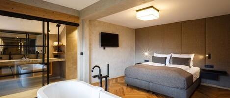 Un dormitorio moderno con una cama grande, una bañera y un televisor en la pared.