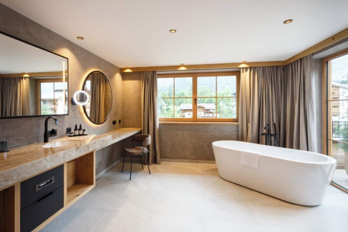 A modern bathroom with a large mirror, a bathtub, and a window with curtains.