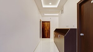 Um corredor com uma porta de madeira identificada com o número '201', um armário de madeira escura e um chão de azulejos brancos.