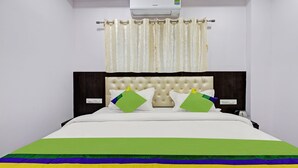 Cama bem arrumada com edredom branco, duas almofadas e um cobertor colorido.