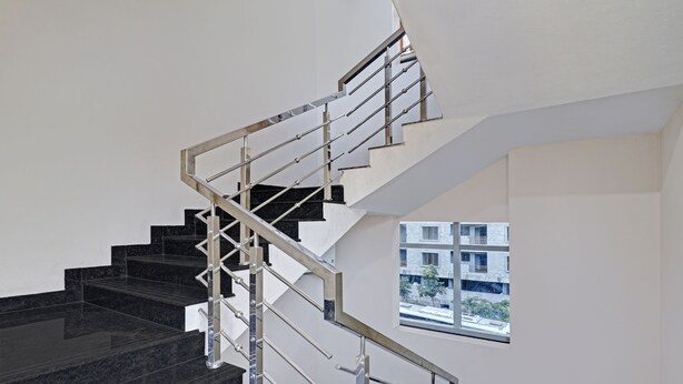 Escadaria moderna com grades de metal e degraus pretos, conduzindo a uma janela com vista para edifícios e árvores.