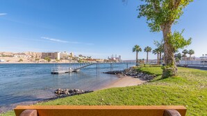 A waterfront park with a wooden bench, a bridge over water, and a cityscape in the background.