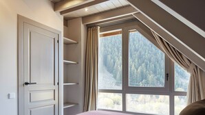 A bedroom with a sloped ceiling, a bed with a pink blanket, a wardrobe, and a large window with curtains. - Val de Ruda Luxe 16 by FeelFree Rentals (Baqueira)