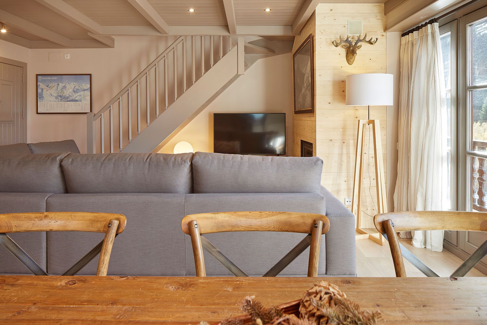 Un salon moderne avec un canapé gris, des chaises en bois, un téléviseur et un escalier.