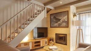 A modern living room with a wooden staircase, a fireplace, a mounted deer head, and a large framed mountain landscape painting. - Val de Ruda Luxe 16 by FeelFree Rentals (Baqueira)