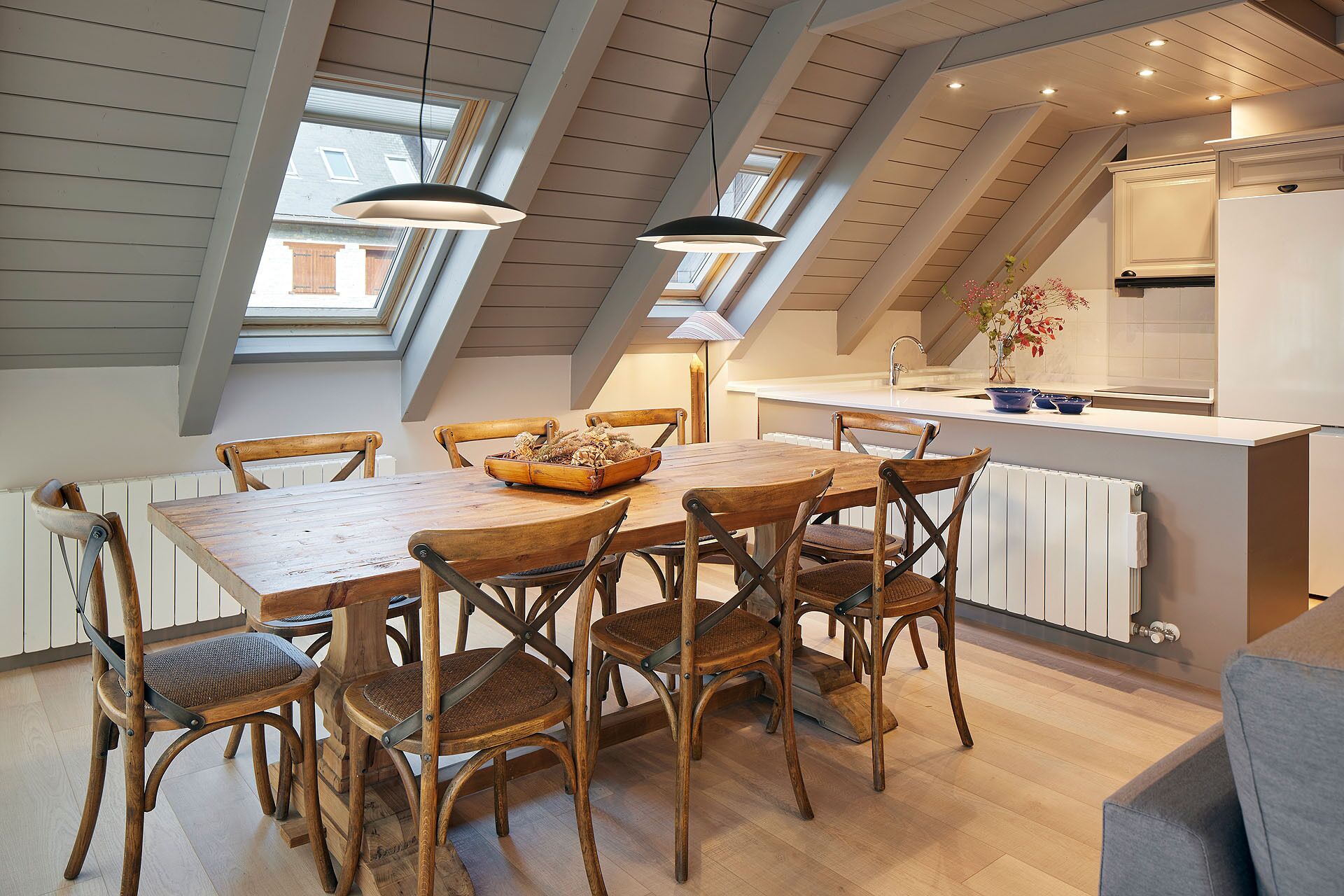 Un coin repas avec une table et des chaises en bois, une cuisine avec un réfrigérateur blanc et des fenêtres de toit.