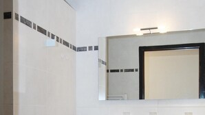 Un baño moderno con azulejos blancos, un espejo grande, un lavamanos con grifo y un mueble con cajones.
