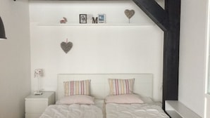 Ein Schlafzimmer mit zwei Betten, einem weißen Nachttisch, einer Ablage mit Dekoration und einem dunklen Holzbalken.