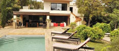 A modern house with a swimming pool, outdoor seating, and a covered patio.
