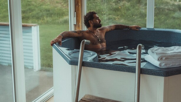 Iemand ontspant in een jacuzzi met uitzicht op een bergachtig landschap door grote ramen.