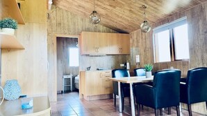 A modern kitchen with wooden cabinets, a dining area with black chairs, and a large window providing natural light. - Hidden Cabin with outdoor hot tub (Ólafsfjordur)