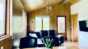 A modern living room with a wooden ceiling, a large window, a sofa set, a table with a plant, and a TV on the wall. - Hidden Cabin with outdoor hot tub (Ólafsfjordur)