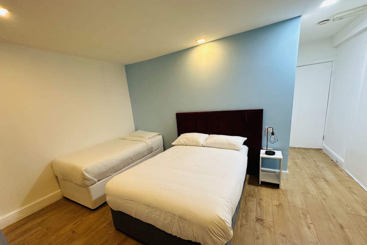 A bedroom with a large bed, a smaller bed, a nightstand, and a wooden floor.
