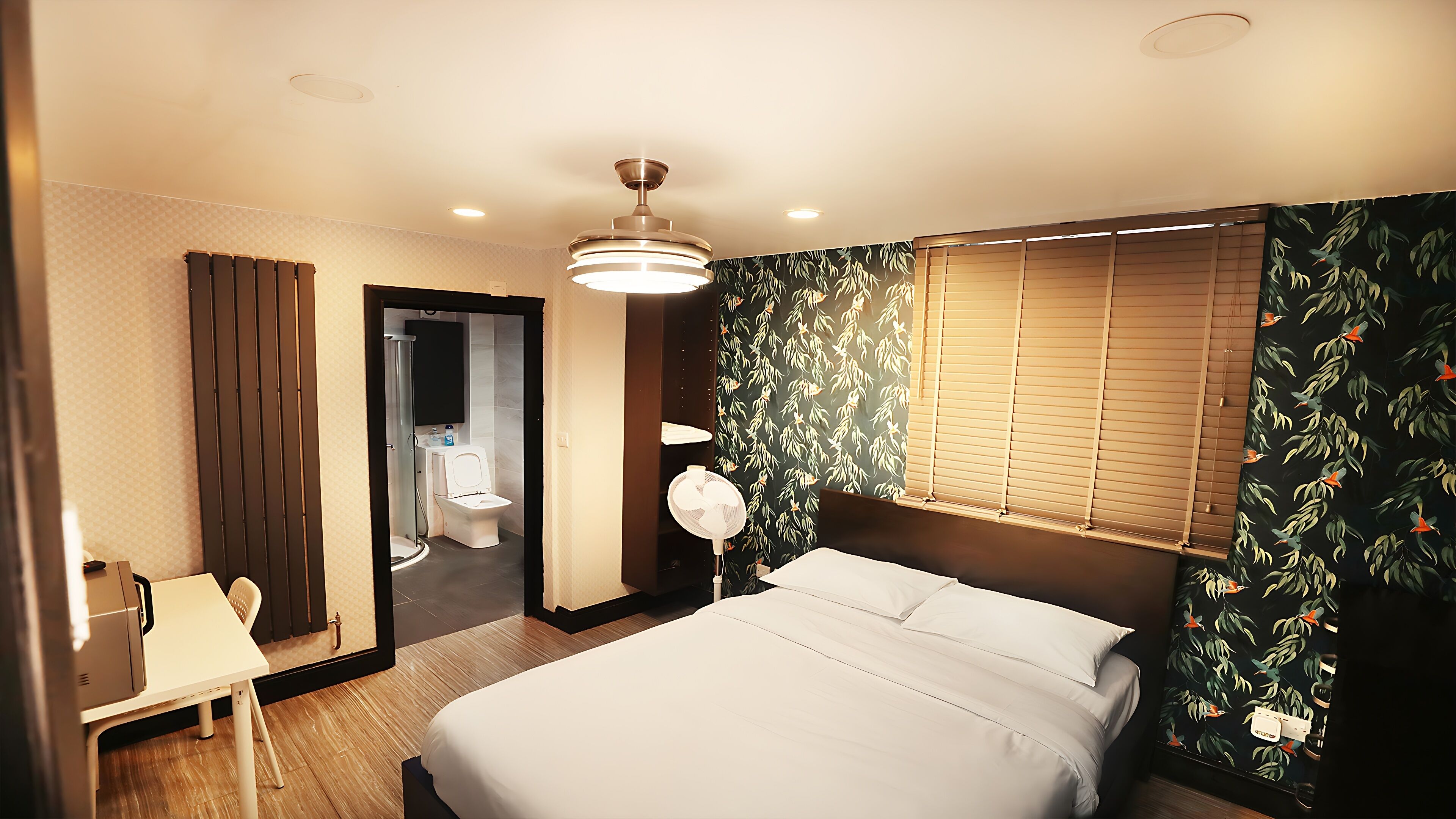 A hotel room with a bed, a desk, a chair, a bathroom, and a window with blinds.