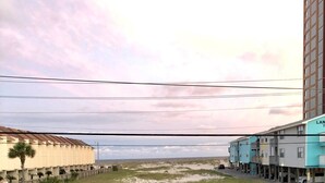 Dos copas de vino blanco sobre un alféizar con vista a una playa y edificios.