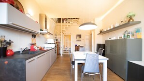 A modern kitchen with a dining area, featuring a central island, white cabinetry, and a staircase leading to an upper level. - Residenza al Pavone Luxury with Terrace (Lucca)