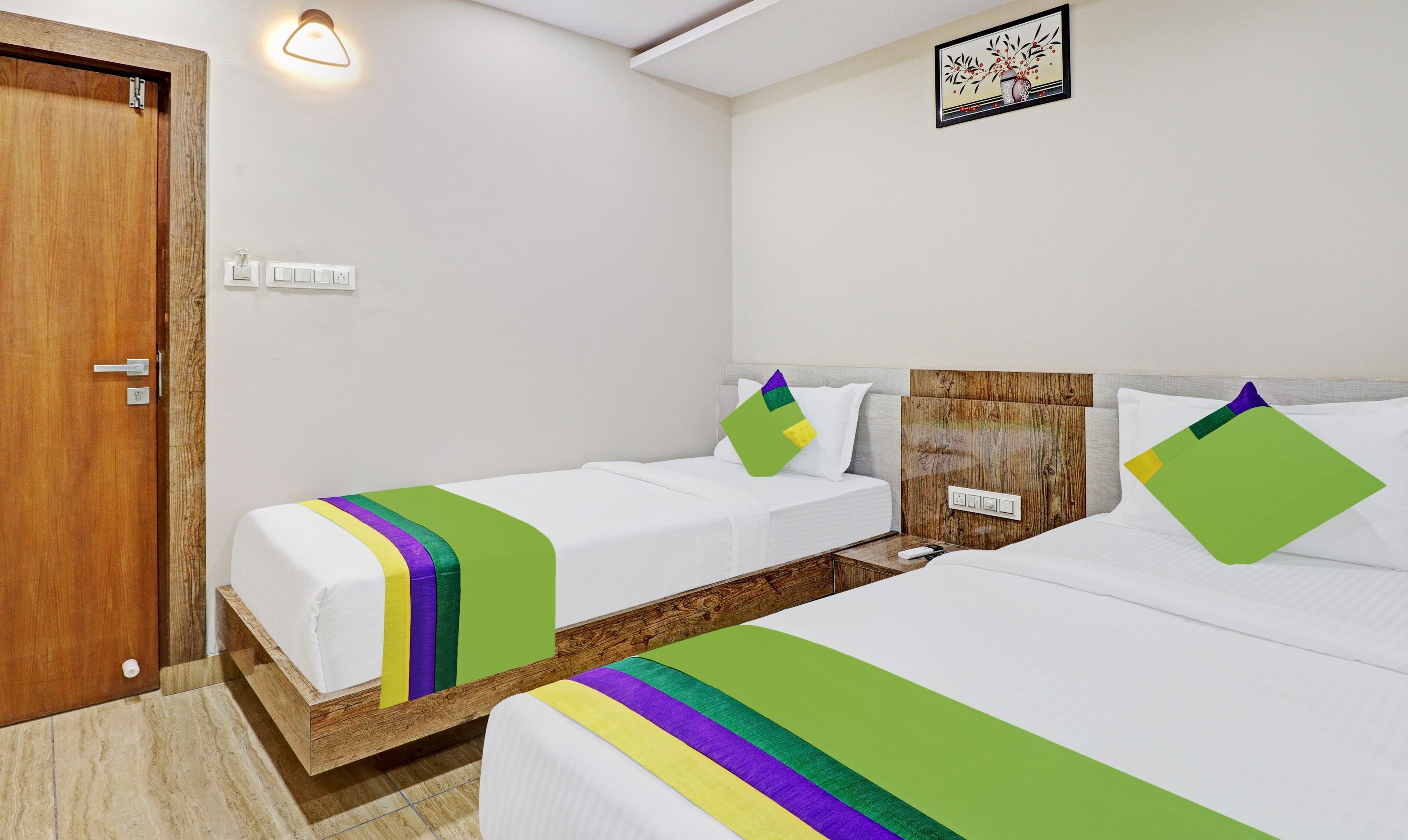 A hotel room with two single beds, a wooden headboard, a wall-mounted light, and a framed picture.