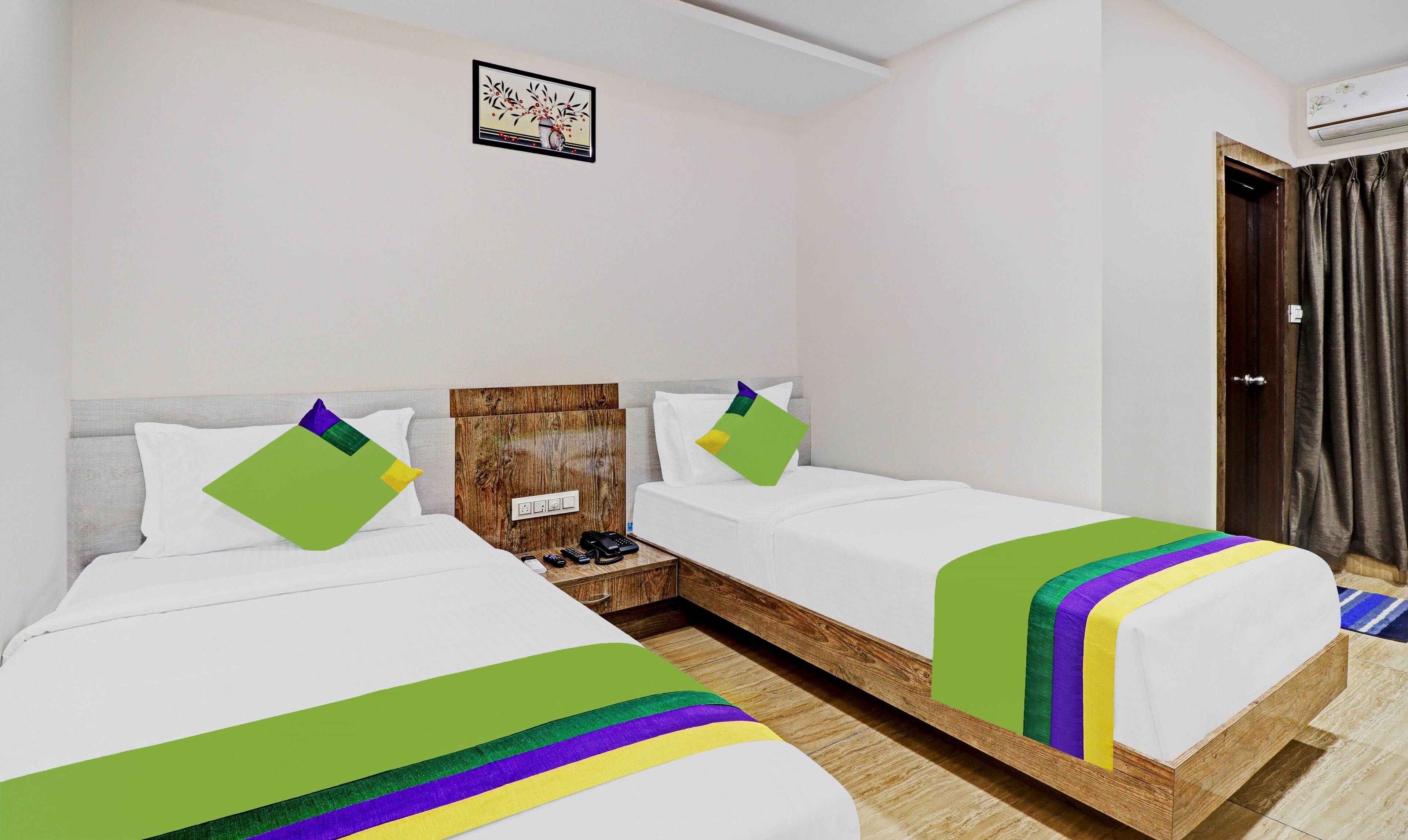 Habitación de hotel con dos camas individuales, cabecera de madera, mesita de noche pequeña con teléfono y un cuadro en la pared.