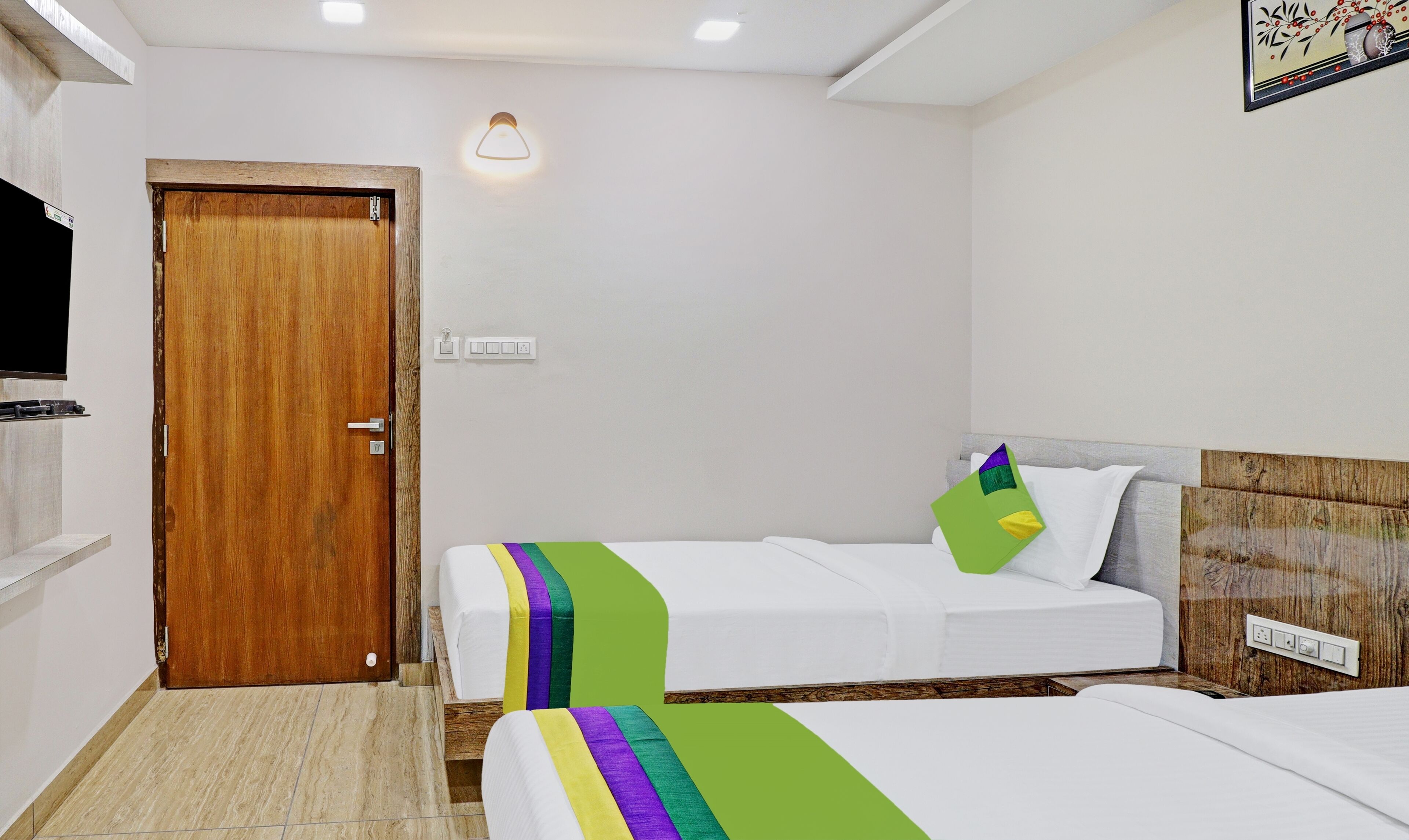 A hotel room with two beds, a wooden door, a wall-mounted light, and a power outlet.