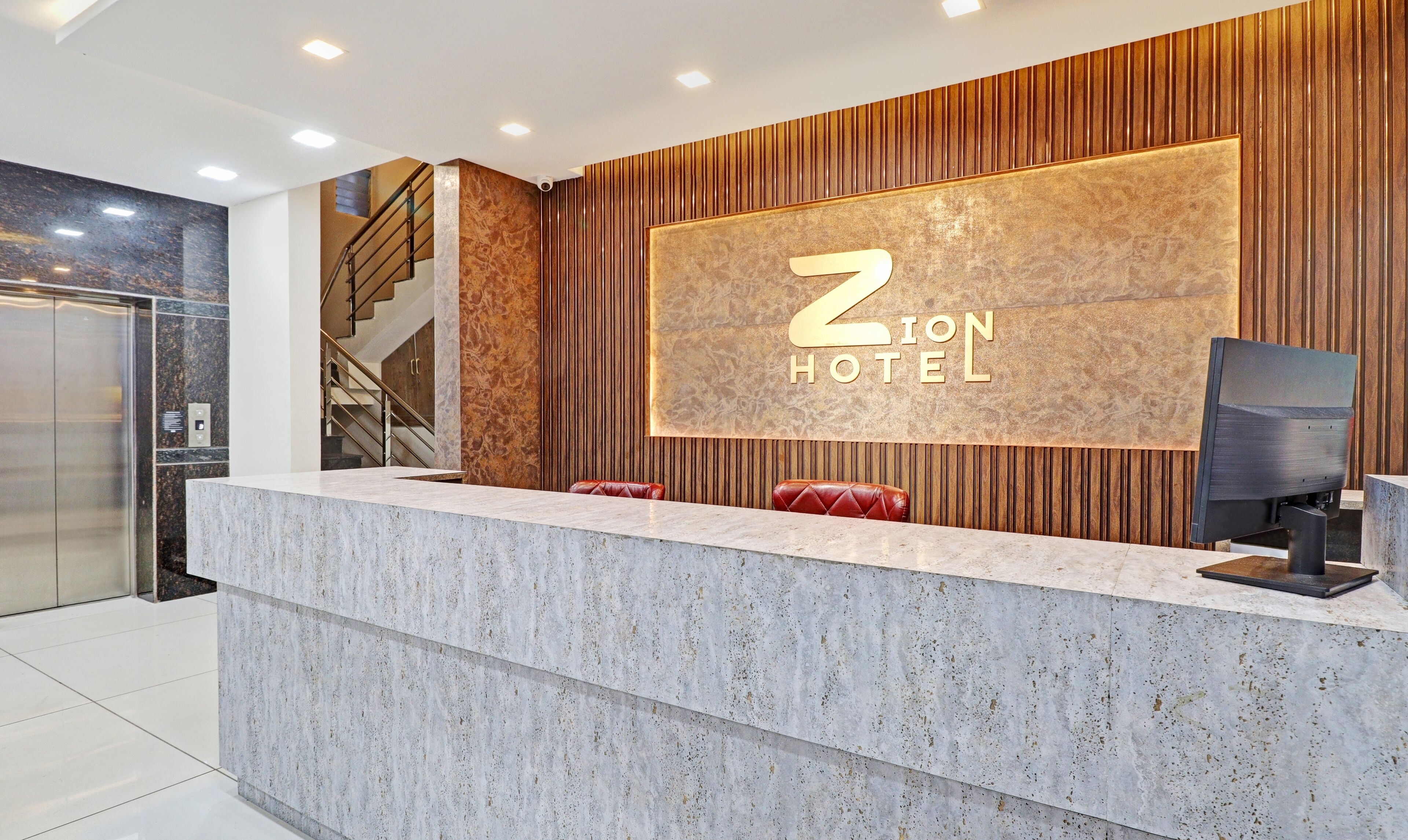 A reception desk with a marble top, a large illuminated sign reading "ZION HOTEL", and a staircase to the left.