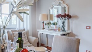 A cozy living room with a white sofa, a dining table with a vase of flowers, a decorative mirror, and a lamp. - Anna Farmhouse Apartment in Wine Resort in Lucca (Monte San quirico)