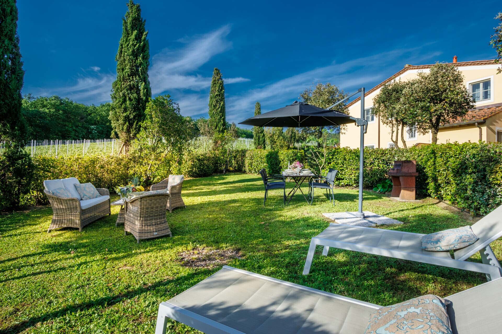 A well-maintained garden with wicker furniture, a dining table, and a lounge chair.