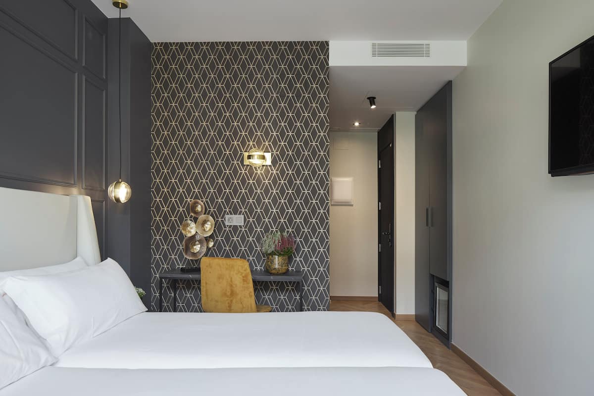 Quarto moderno com uma cama grande, uma escrivaninha com cadeira, televisão fixada na parede e um painel decorativo.