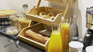 Un bufé de desayuno con pasteles, cereales y vasos de jugo en una barra.