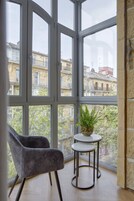 Una habitación con ventanas amplias, una silla gris y una mesita con una planta.