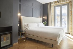 Un dormitorio moderno con una cama grande, una mesita de noche pequeña, televisión integrada y vistas a la ciudad desde la ventana.