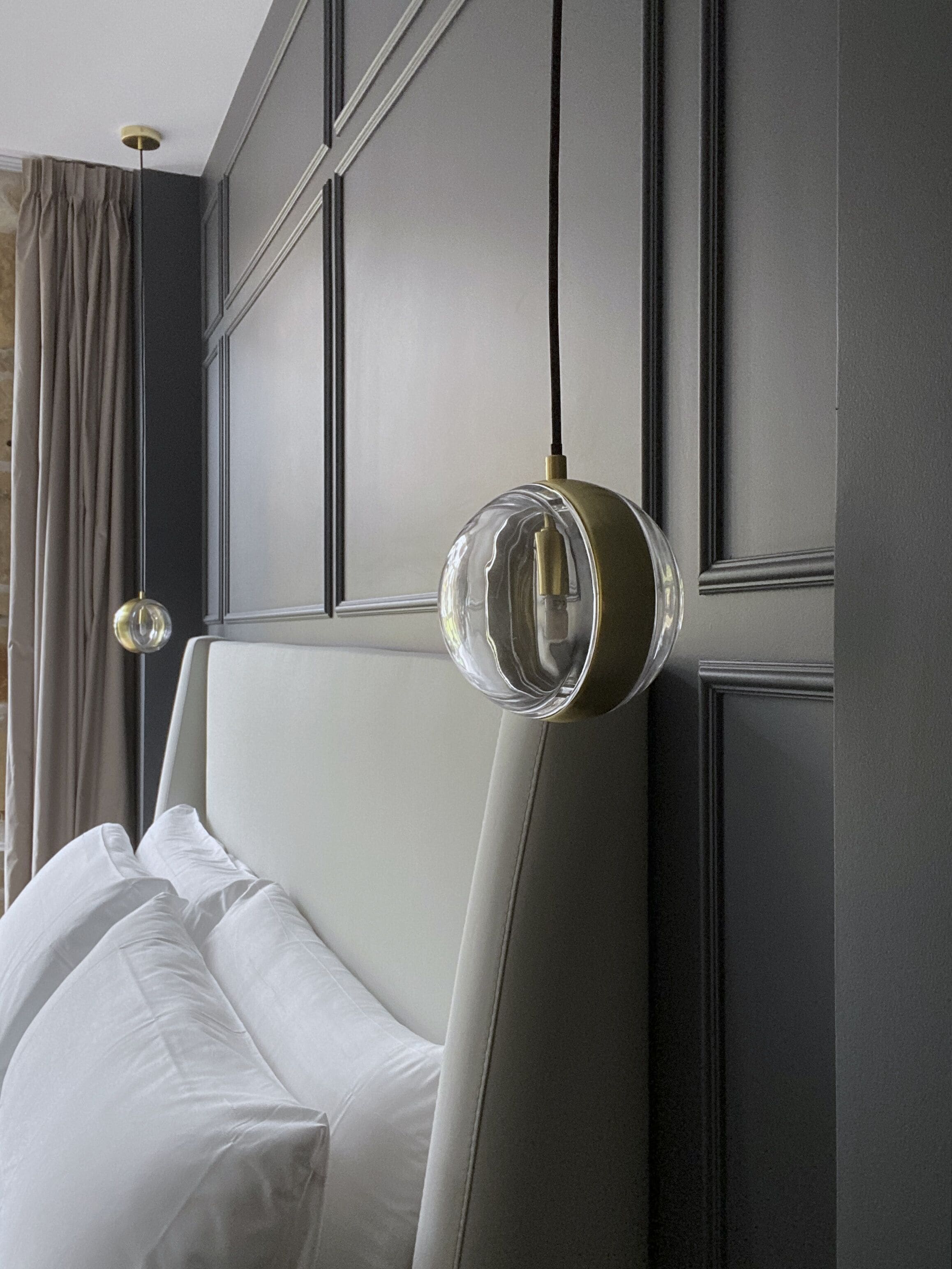 Habitación de hotel moderna con una cama grande, una lámpara colgante redonda y vistas de la ciudad.