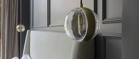 A modern hotel room with a large bed, a round pendant light, and a view of the city.