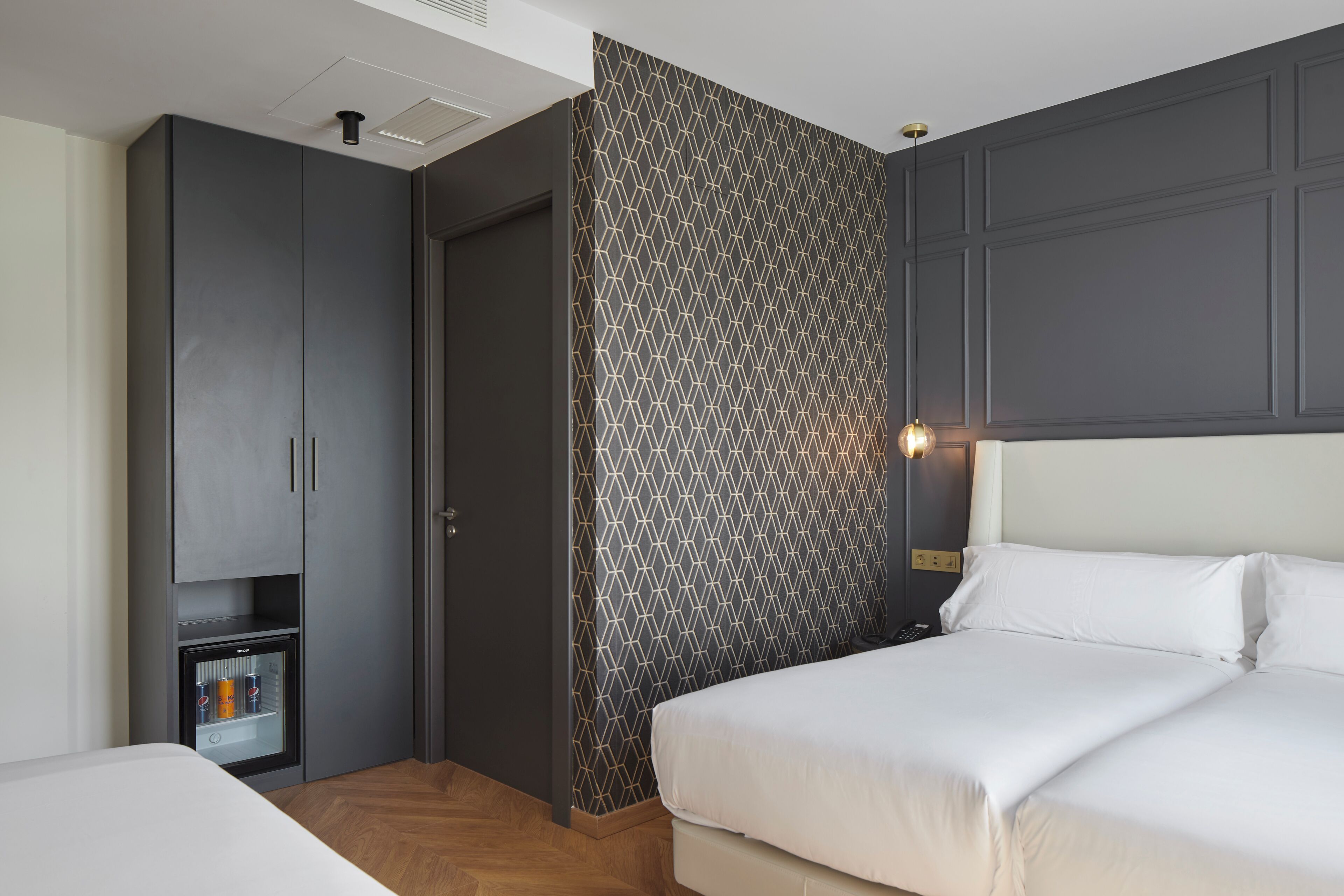 A hotel room with a bed, a wardrobe, a mini-fridge, and a patterned wall.