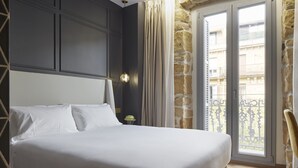 Habitación de hotel con una cama grande, una mesita de noche, una lámpara y vistas al balcón exterior.